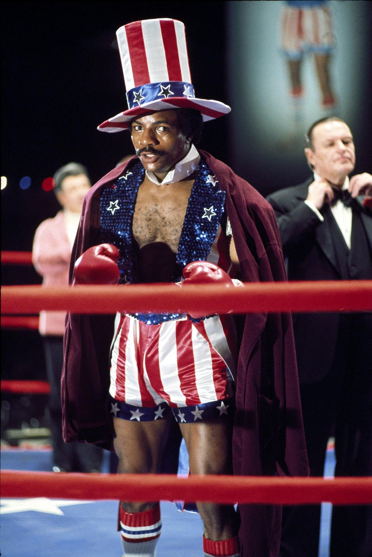 Ein Boxer im US-Flaggenkostüm mit Zylinder steht im Ring, rote Boxhandschuhe bereit.
