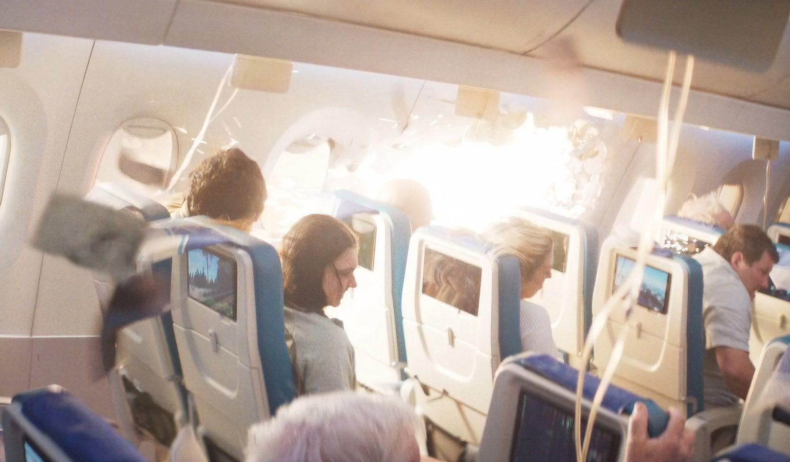 Passagiere sitzen in Flugzeugsitzen mit integrierten Bildschirmen; helles Licht scheint herein.