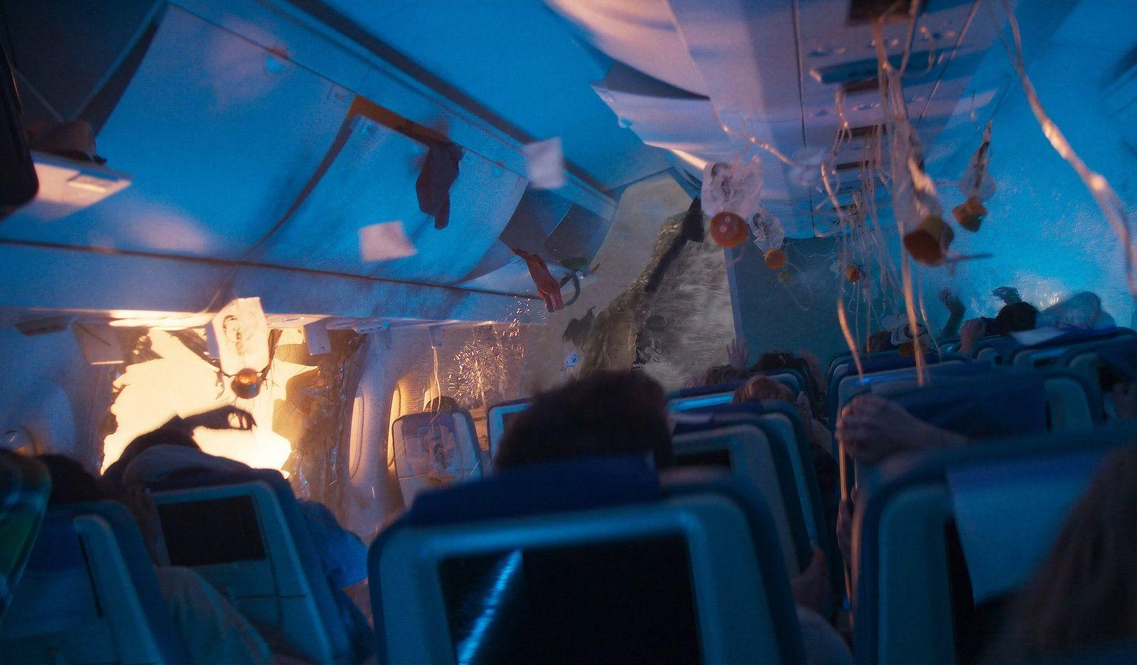 Chaos im Flugzeuginnenraum mit herabhängenden Sauerstoffmasken, Passagieren und starker Beschädigung.