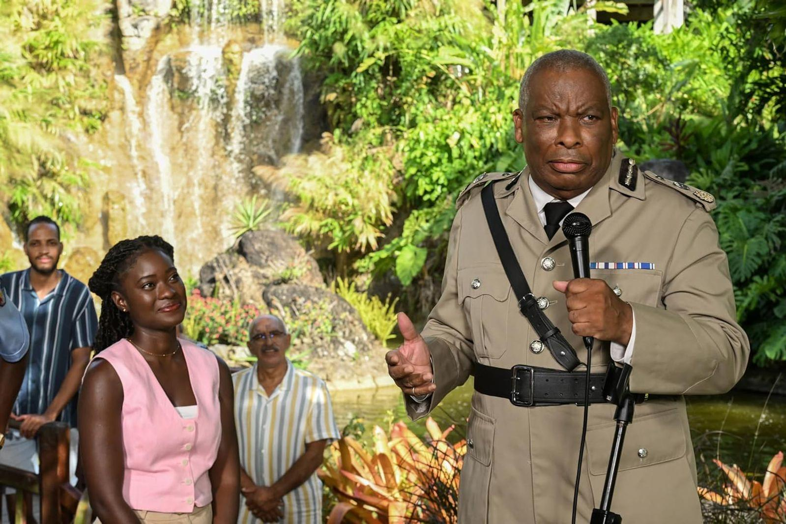 Ein Polizeibeamter in Uniform spricht im Freien vor einem Wasserfall in ein Mikrofon.