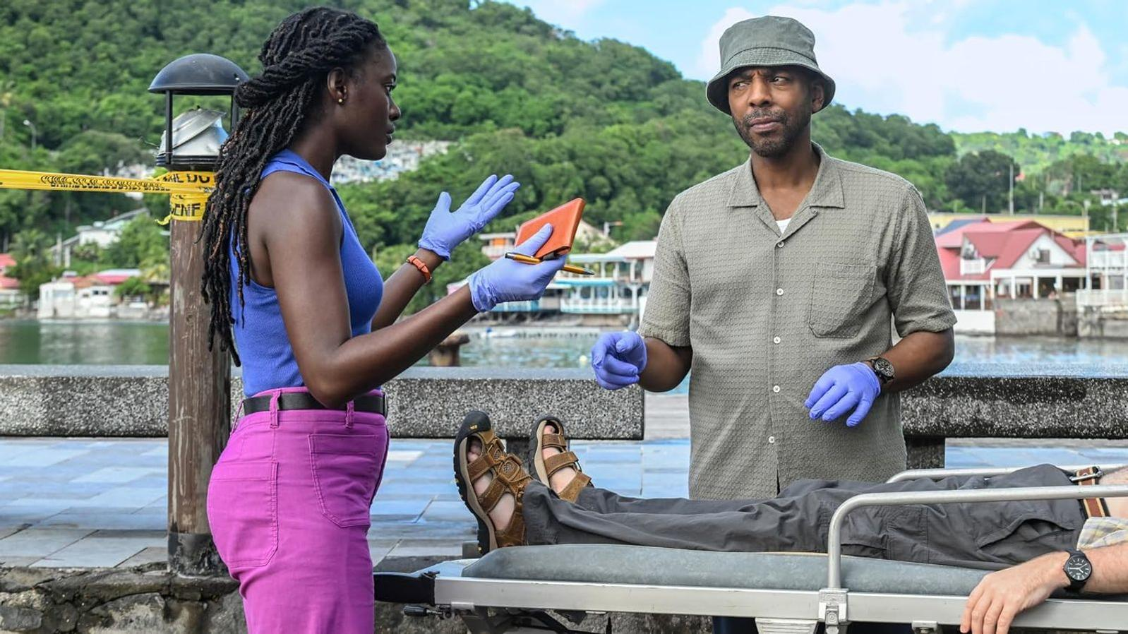 Ermittler in blauen Handschuhen stehen am Tatort neben einer Trage und sprechen.