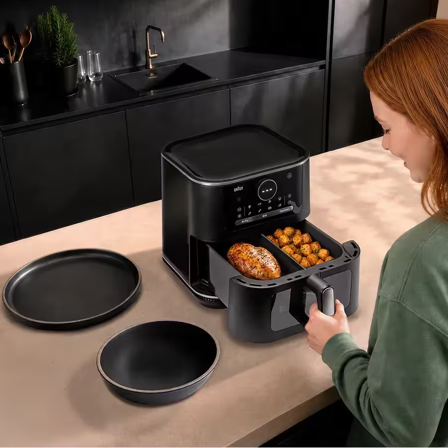 Una donna apre il doppio cassetto di una friggitrice ad aria nera con pollo e patate.