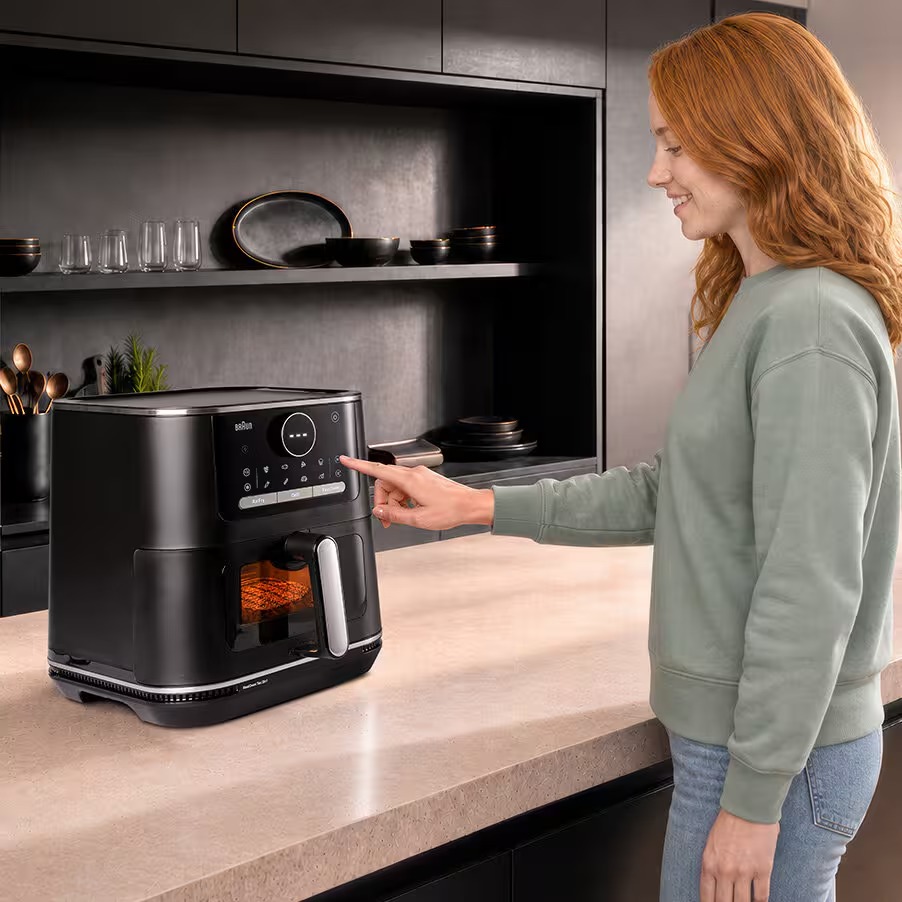 Una donna con una felpa verde usa il touchscreen di una friggitrice ad aria nera su un piano cucina.