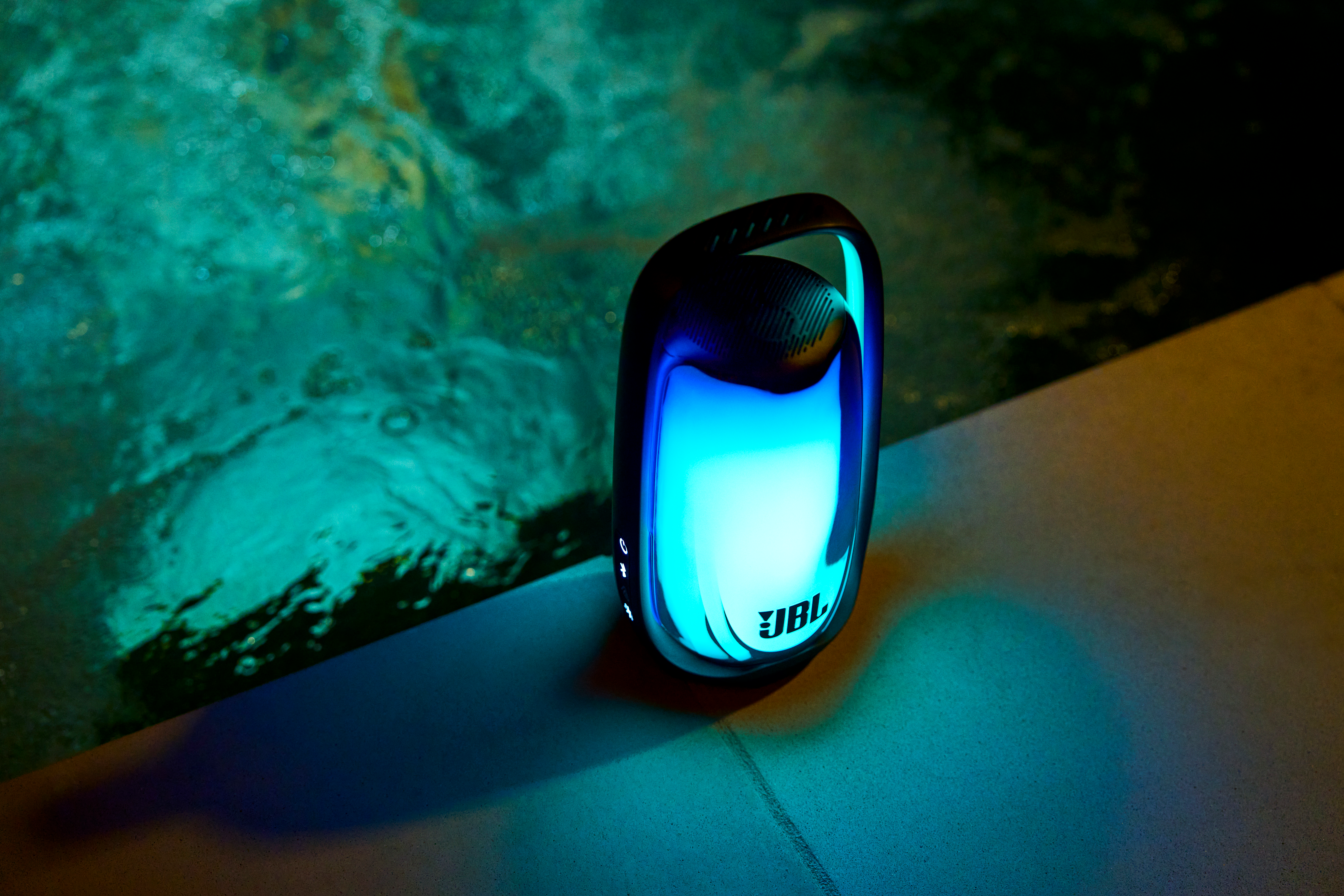 Une enceinte JBL illuminée repose au bord d'une piscine la nuit.
