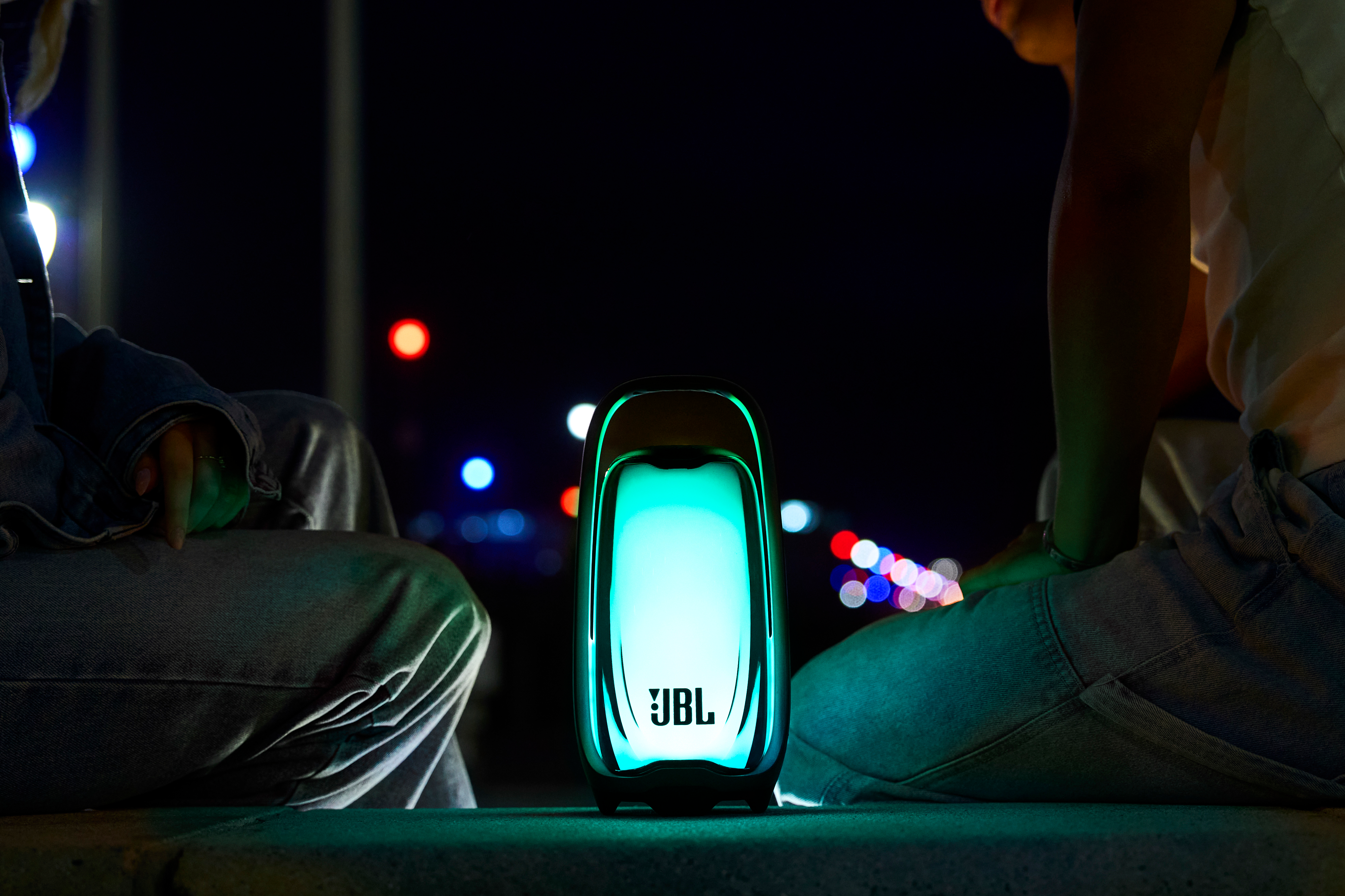 Enceinte JBL éclairée dans une rue sombre la nuit avec deux personnes en arrière-plan.