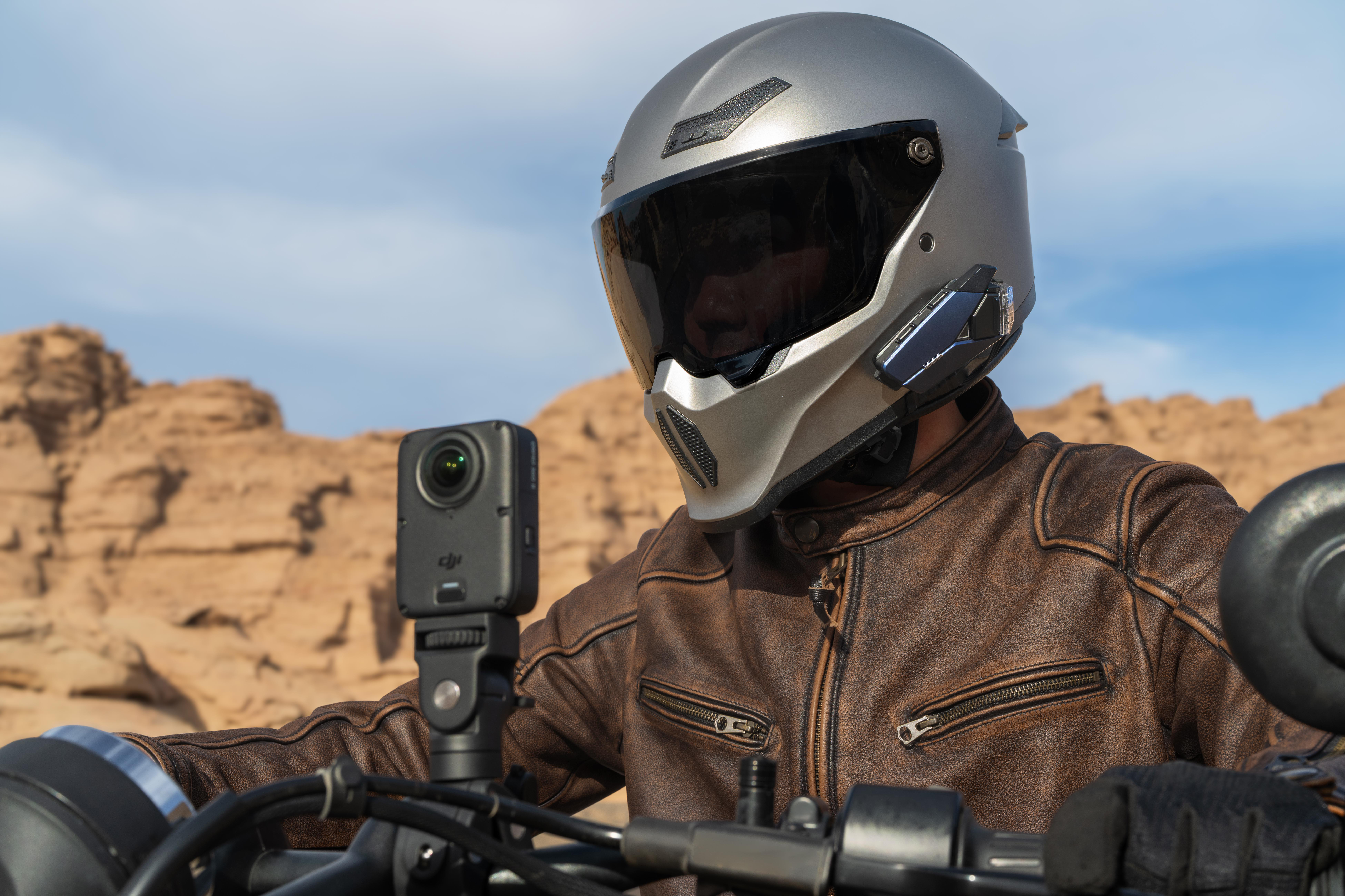 Motorradfahrer in brauner Lederjacke und silbernem Helm mit Action-Kamera am Lenker.