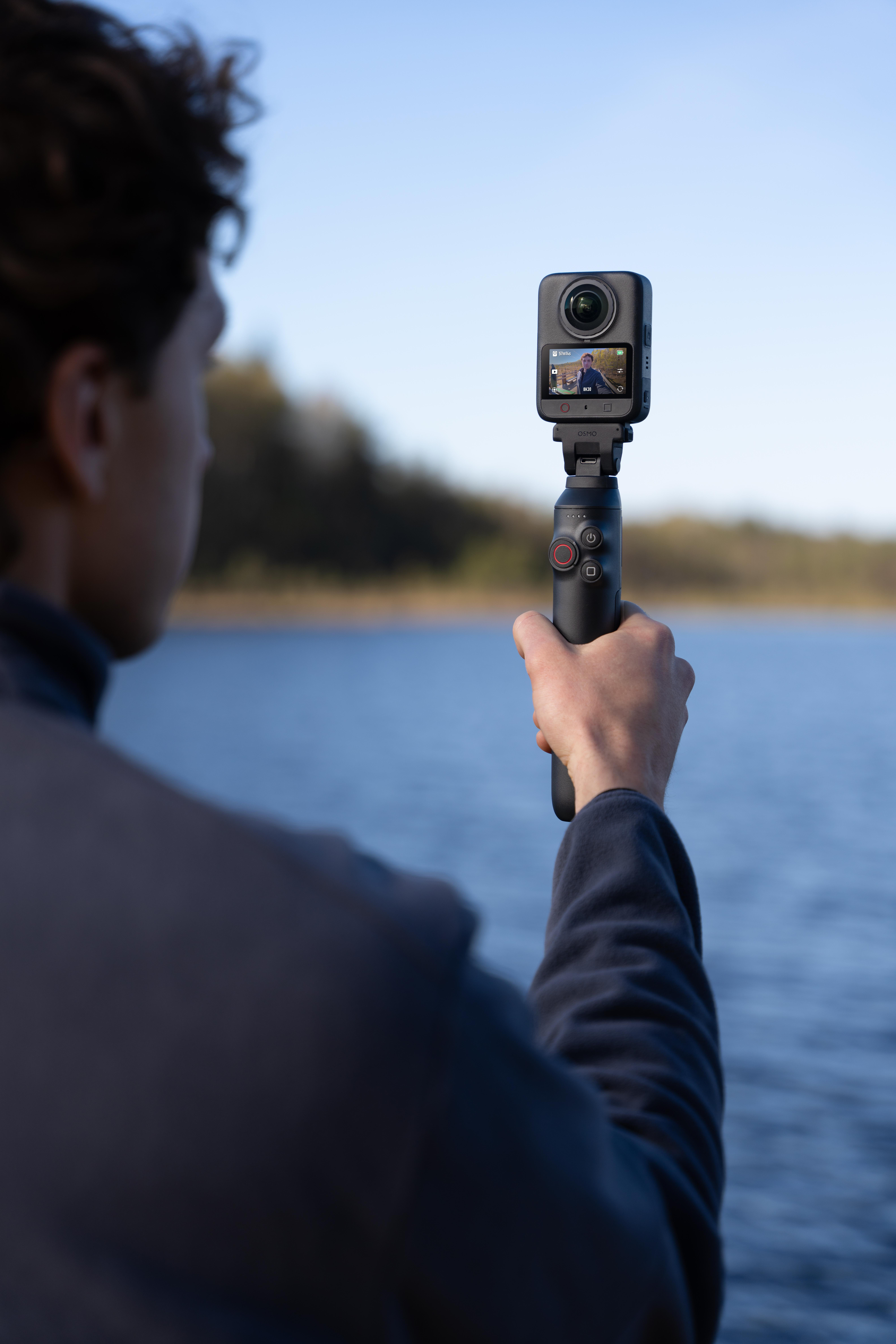 Eine Person hält eine kleine Gimbal-Kamera mit Bildschirm vor einer Flusslandschaft.