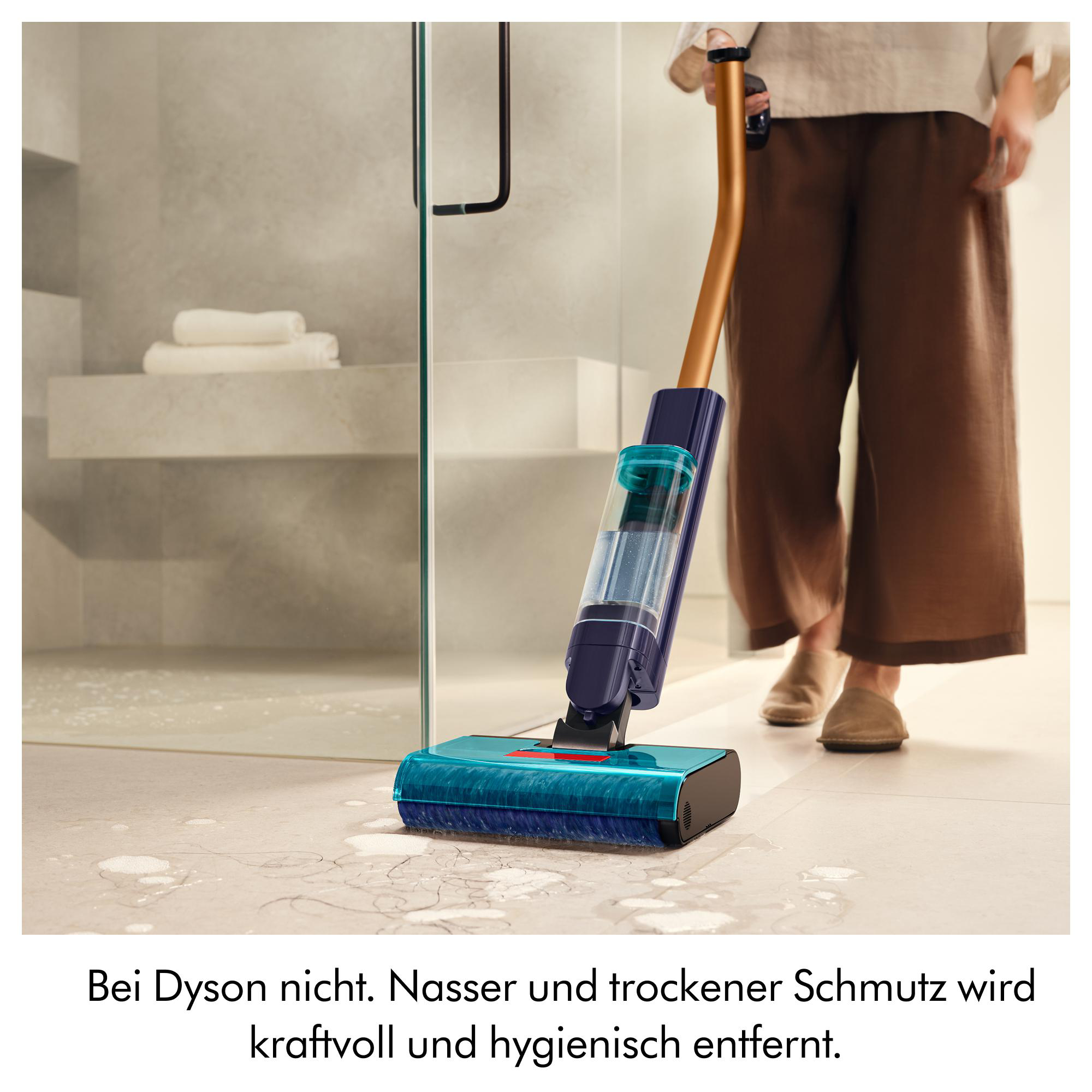 Eine Person nutzt einen blauen Dyson-Bodenwischer auf hellem Fliesenboden vor einer Glasdusche.