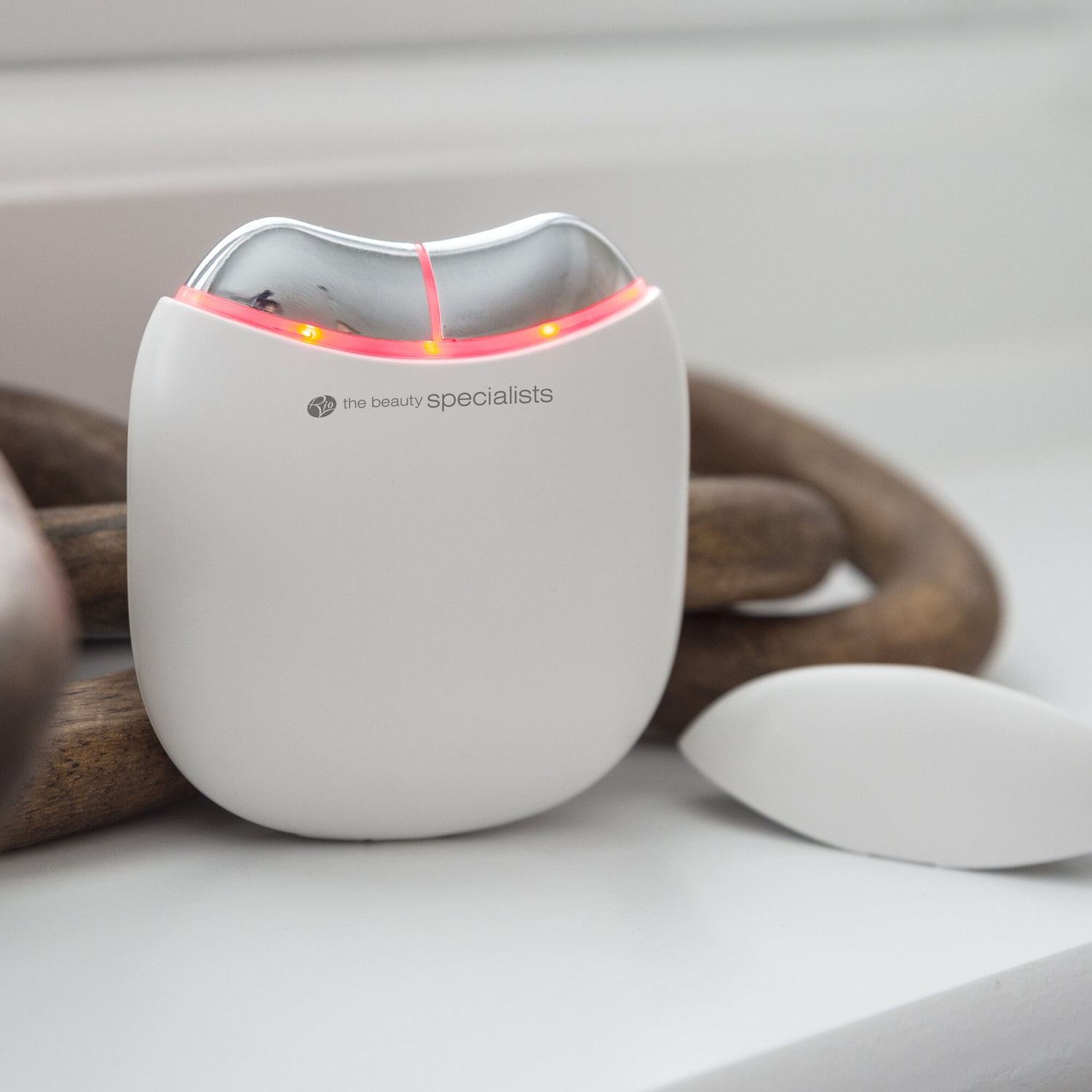 Dispositivo di bellezza bianco con parte superiore argentata e luci LED rosse, posizionato su una superficie chiara.