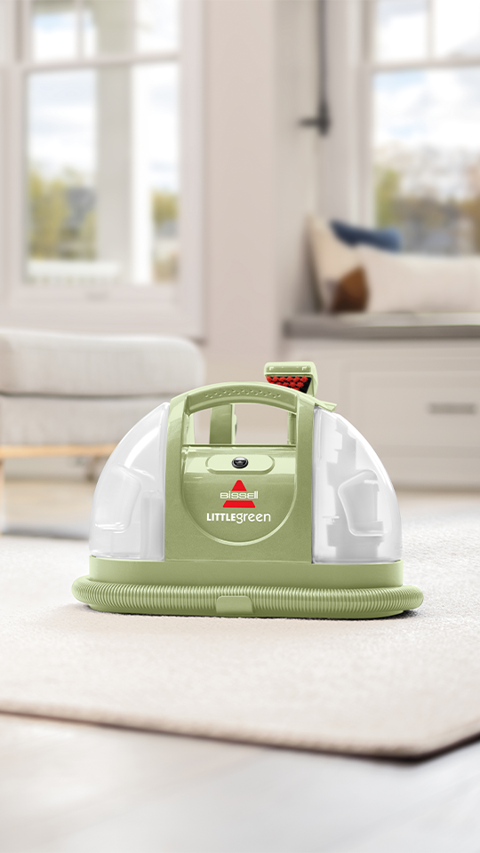 Yeşil renkli taşınabilir Bissell Little Green halı temizleyici, odadaki açık renkli bir halının üzerinde duruyor.