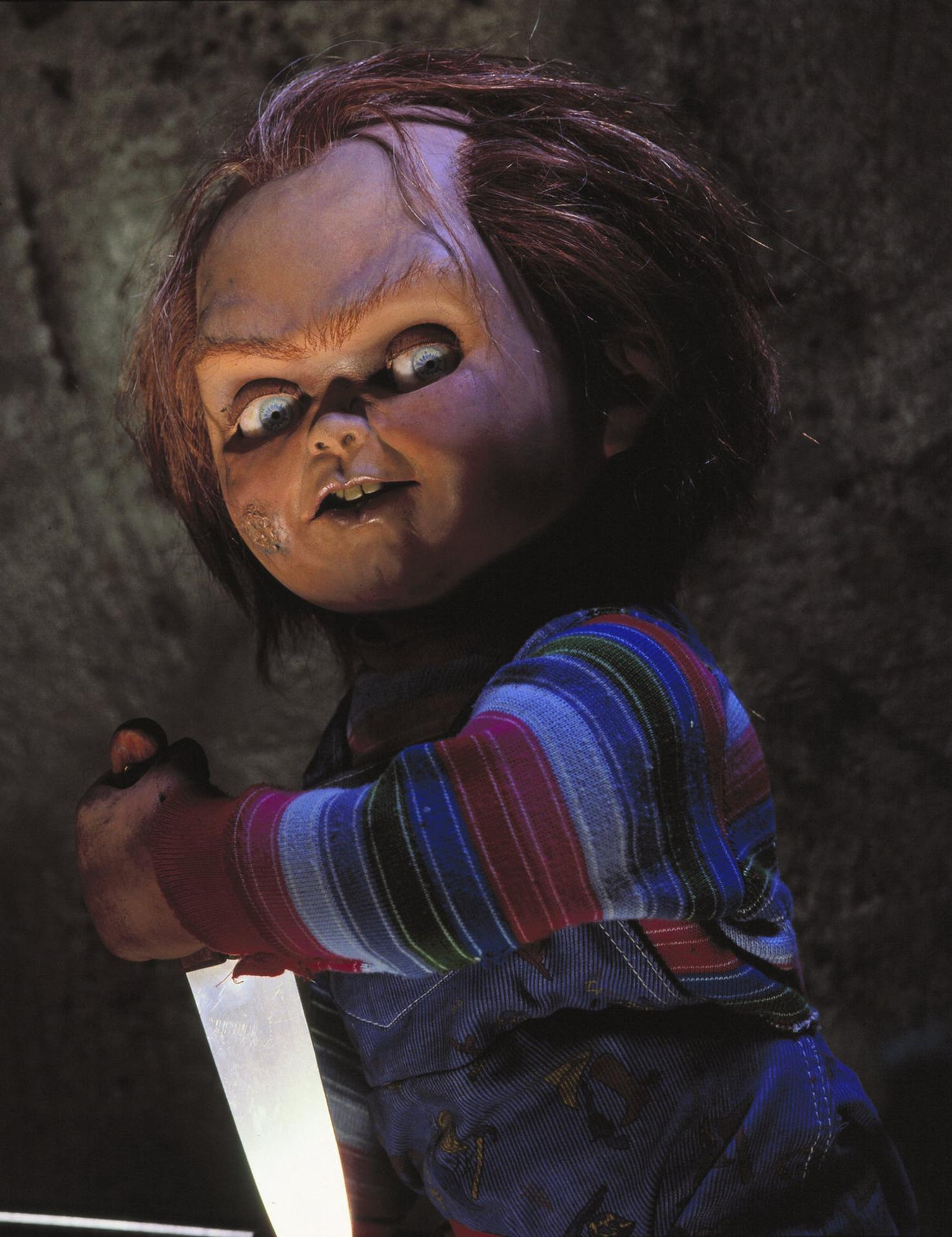 Nahaufnahme der Chucky-Puppe, die in gedimmtem Licht ein Messer hält.