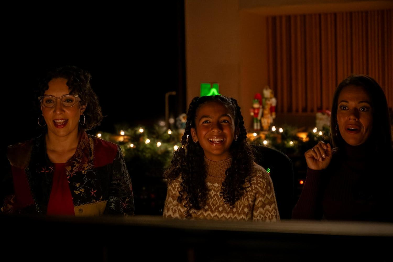 Drei Frauen schauen mit erstaunten und fröhlichen Gesichtern auf eine Bühne, umgeben von warmer Weihnachtsbeleuchtung.