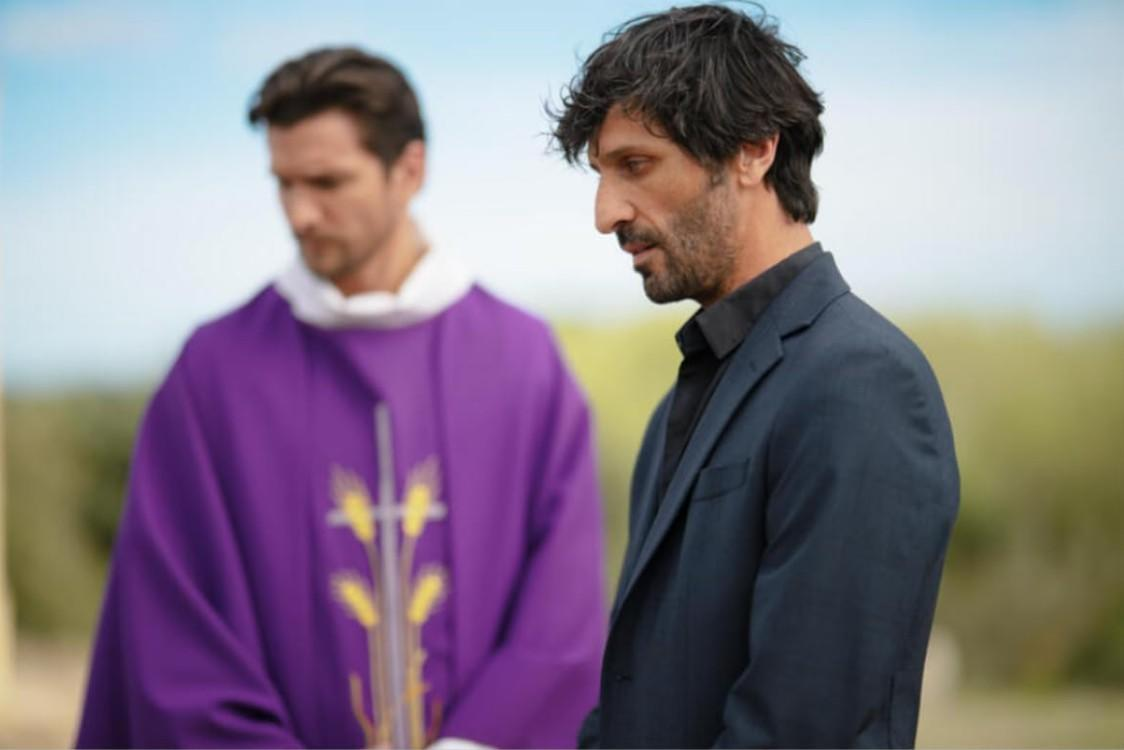 Ein Mann im dunklen Anzug steht neben einem Priester in violettem Gewand.
