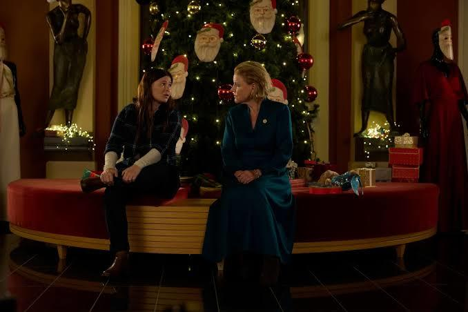 Zwei Frauen sitzen vor einem Weihnachtsbaum auf einer roten Bank in einem Raum mit Schaufensterpuppen.