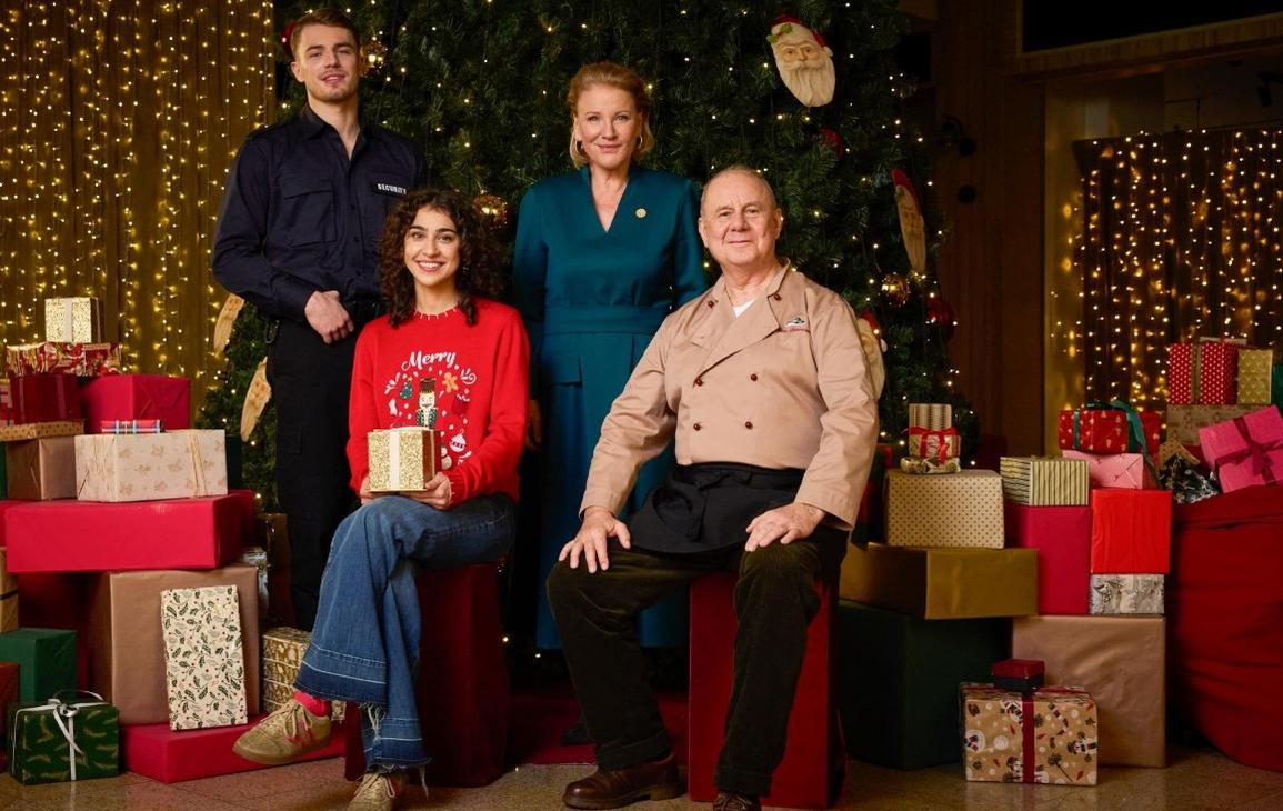 Vier Personen posieren vor einem Weihnachtsbaum und vielen Geschenken.