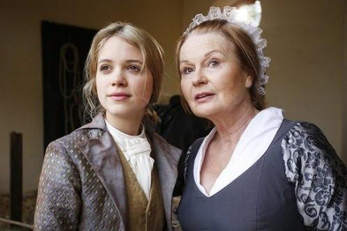 Zwei Frauen in historischer Kleidung, eine junge Blondine in einer Jacke und eine ältere Frau mit Häubchen.