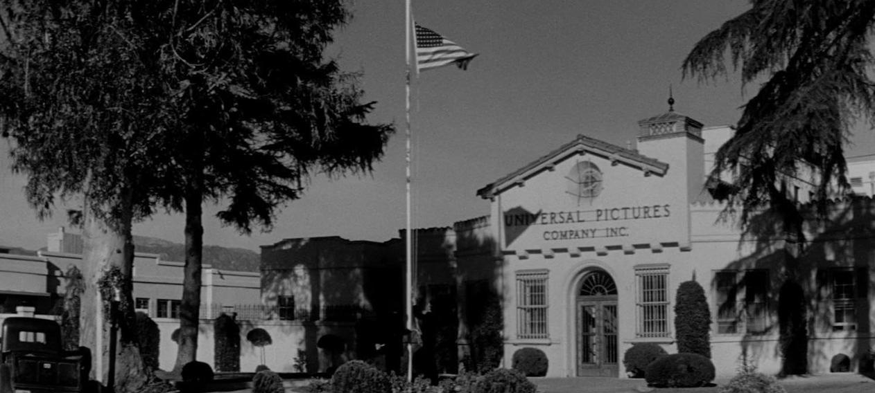 Schwarz-Weiß-Ansicht des Gebäudes der Universal Pictures Company Inc. mit Bäumen und einer amerikanischen Flagge.