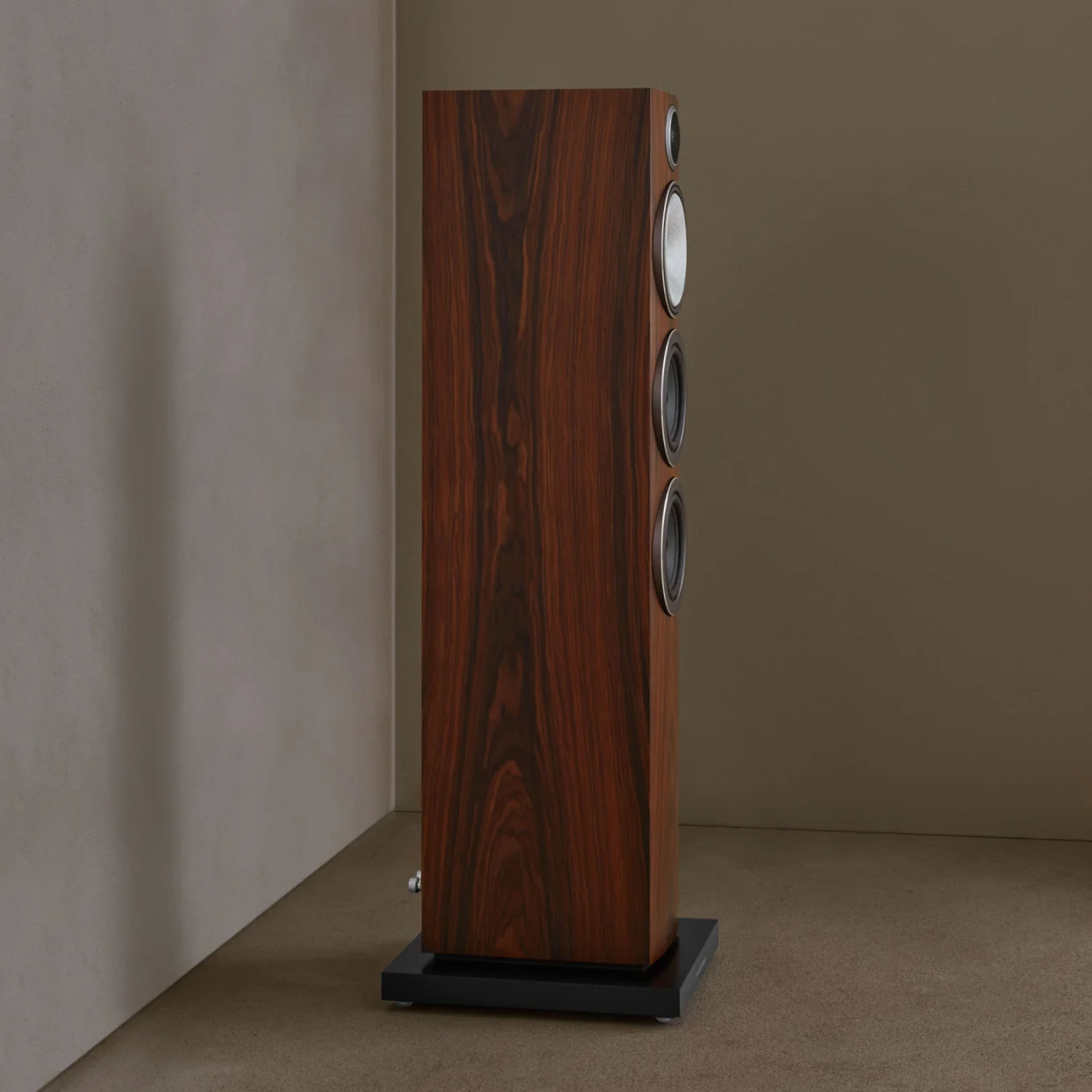 Ein großer Standlautsprecher aus Holz steht aufrecht in einer Ecke an einer schlichten Wand.