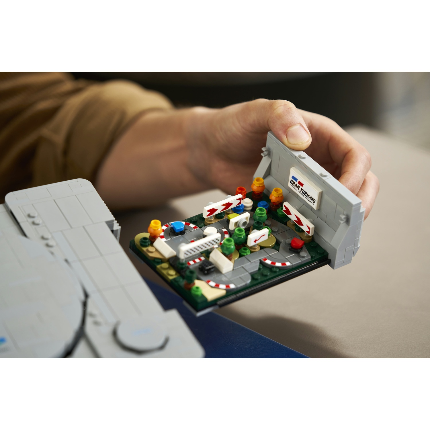Una mano apre un modello LEGO rivelando una pista da corsa in miniatura con auto e barriere.