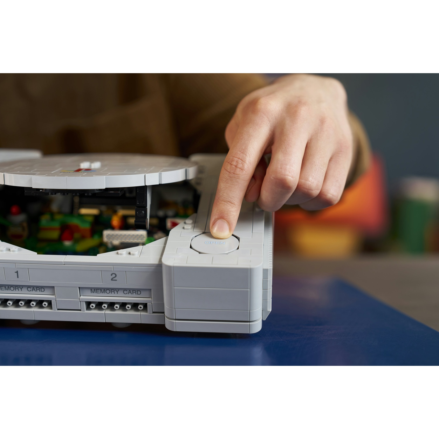 Una mano preme il pulsante di apertura su una console di gioco grigia in Lego.