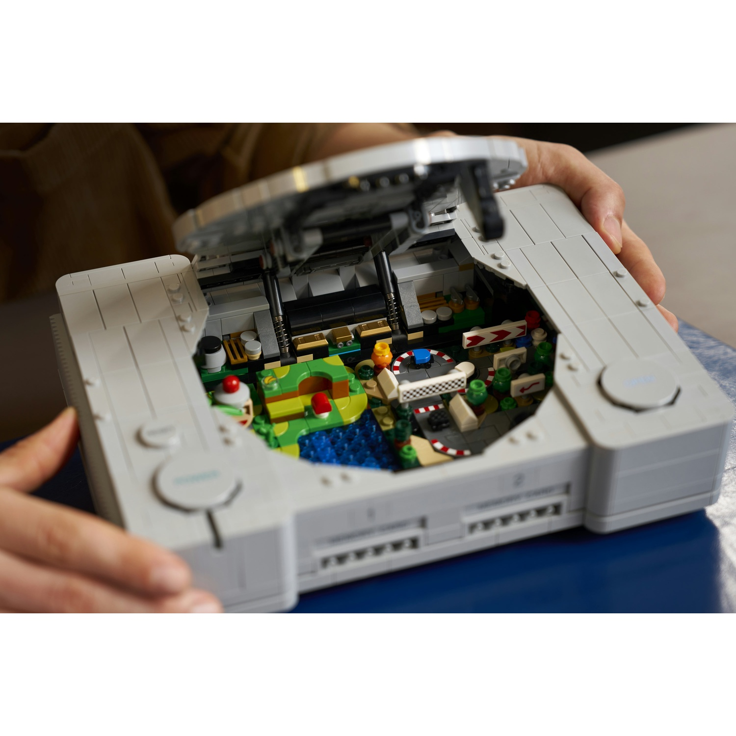 Una console di gioco Lego grigia con il coperchio aperto rivela un gioco di corse in miniatura con paesaggio.