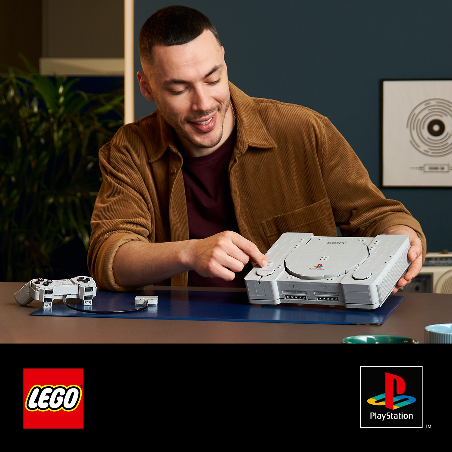 Un uomo con una camicia marrone preme il pulsante di una console PlayStation in mattoncini LEGO.