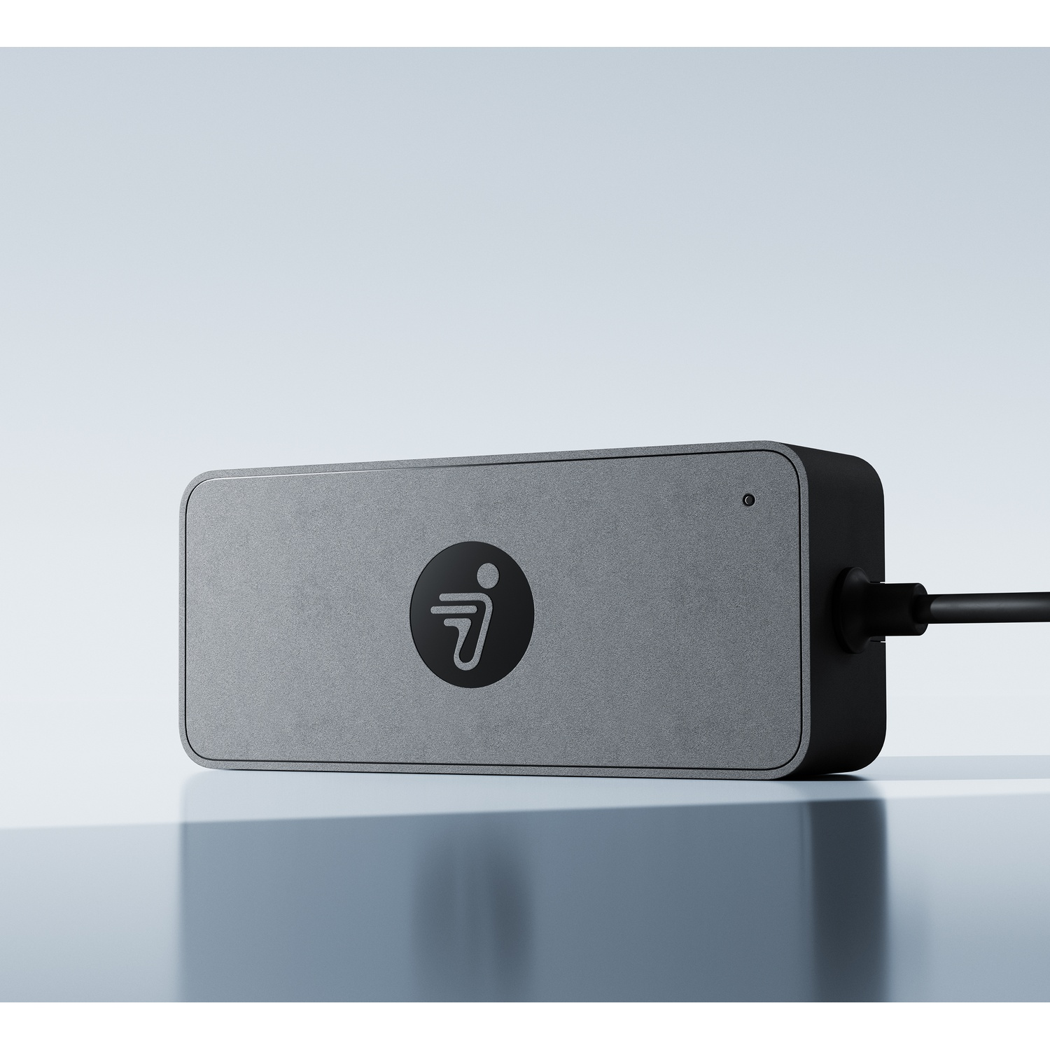 Un appareil rectangulaire gris avec un logo rond et un câble connecté sur une surface brillante.