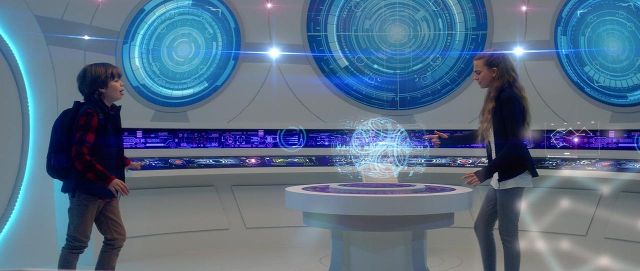 Ein Junge und ein Mädchen stehen in einem futuristischen Kontrollraum mit blau leuchtenden Hologrammen.