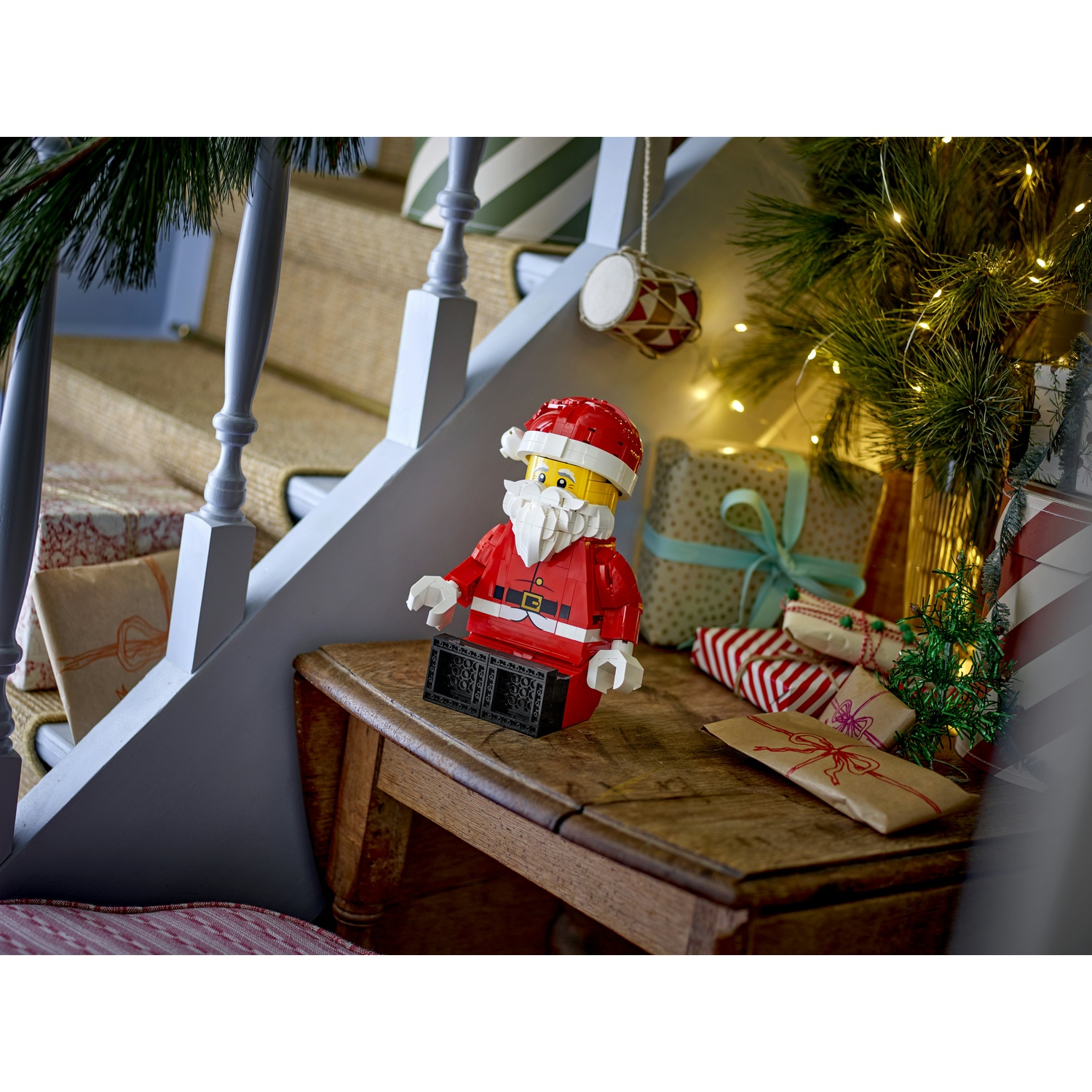 Una statuetta di Babbo Natale Lego siede su un tavolo di legno, circondata da regali e un albero di Natale.