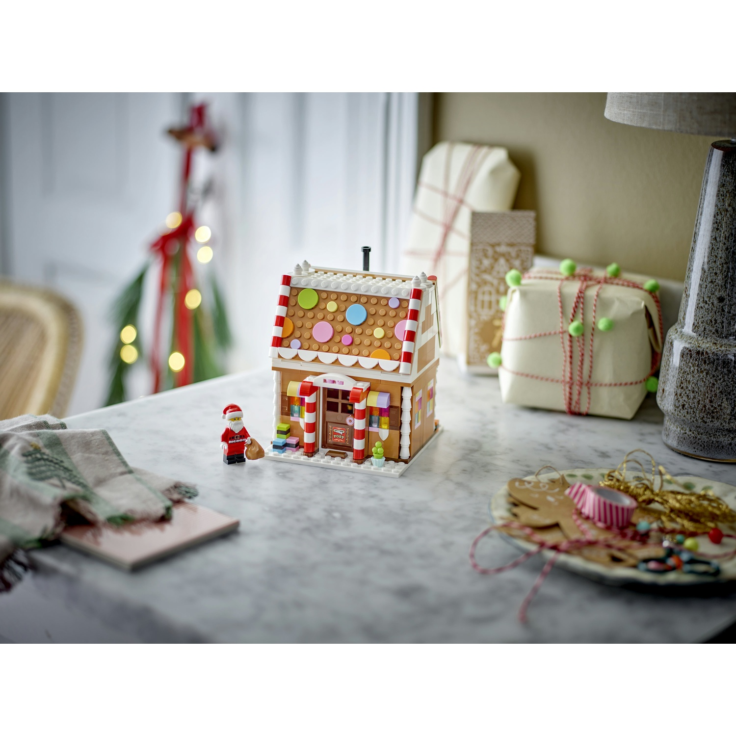 Una casetta di marzapane Lego con decorazioni colorate su un tavolo di marmo, accanto a una statuetta di Babbo Natale.