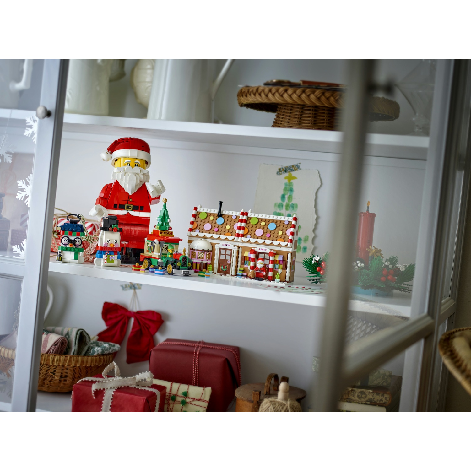 Un ripiano di un mobile bianco mostra statuette di Natale Lego, una casa di pan di zenzero e regali.