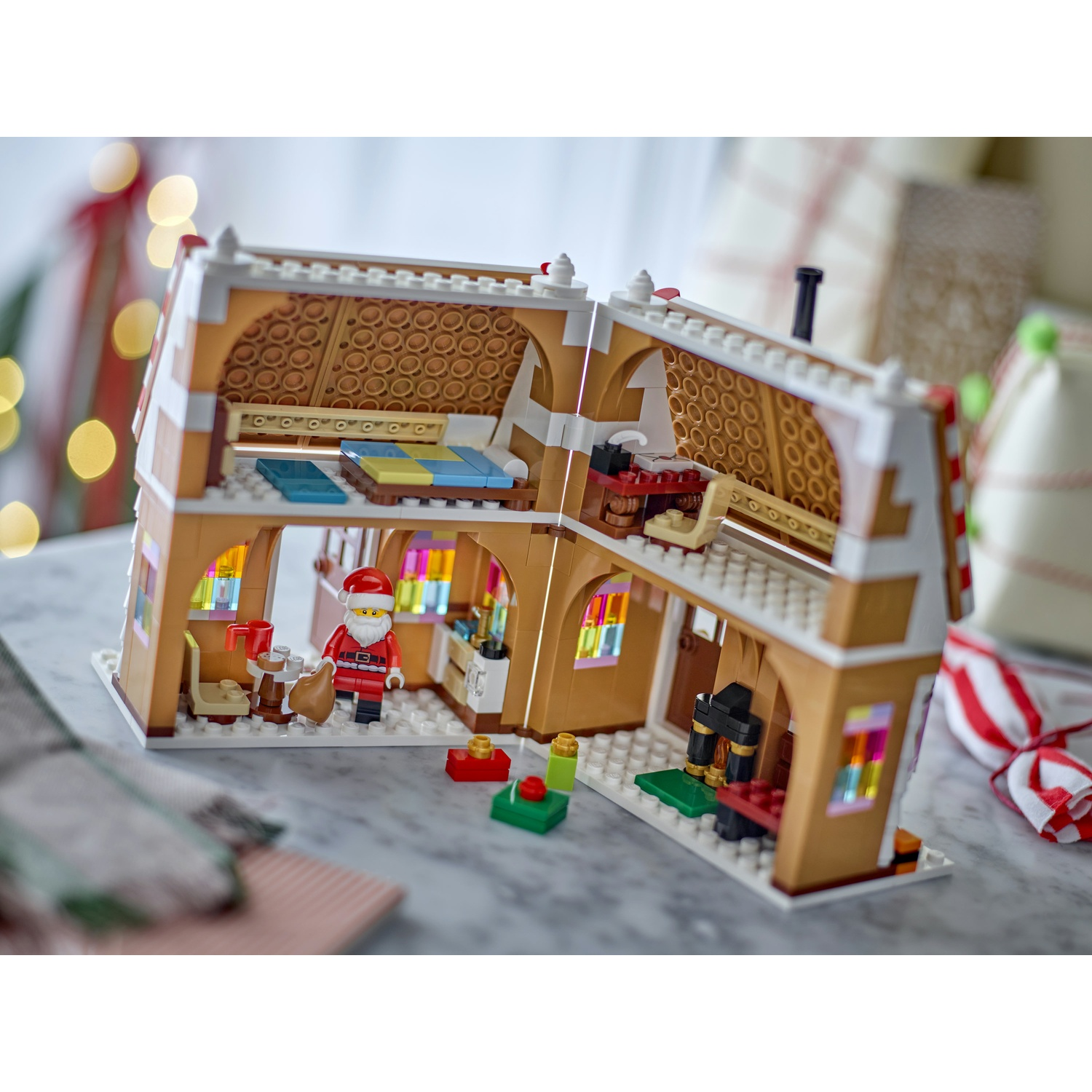 Una casa di pan di zenzero Lego con tetto aperto, statuetta di Babbo Natale e finestre colorate.