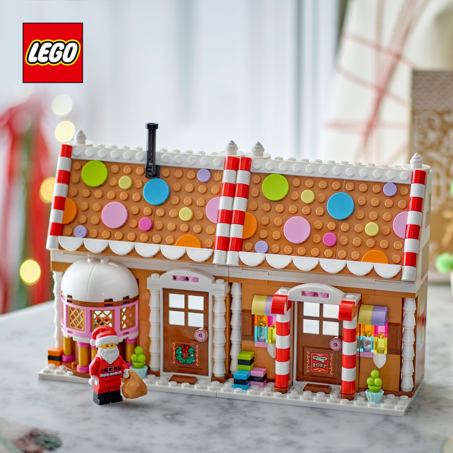 Casetta di pan di zenzero LEGO con colonne a righe, tegole colorate sul tetto e una minifigura di Babbo Natale.