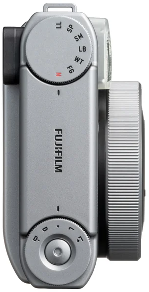 Egy ezüst Fujifilm kamera felülnézete tárcsákkal, exponálógombbal és objektívvel.