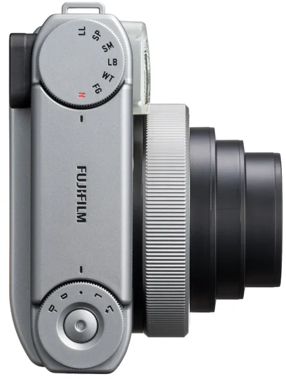 Ezüstszínű Fujifilm kamera felülnézete, kinyújtott fekete objektívvel és kezelőszervekkel.