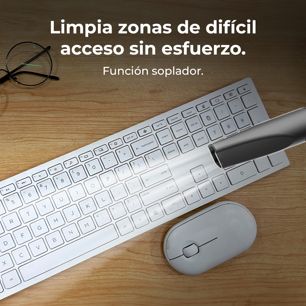 Una boquilla de miniaspiradora limpia un teclado y ratón blancos en un escritorio de madera.