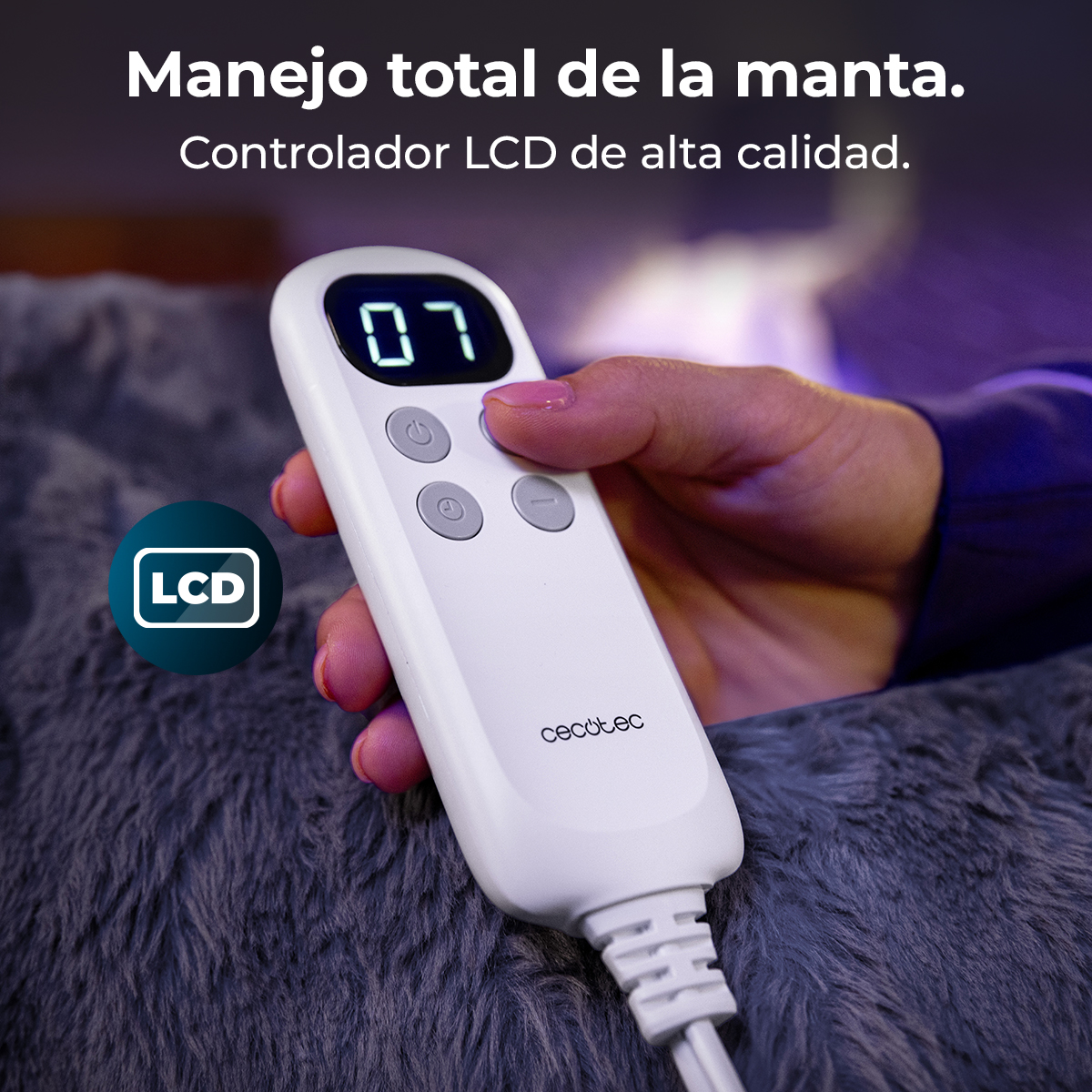 Una mano sostiene un control remoto LCD blanco sobre una manta gris con texto.