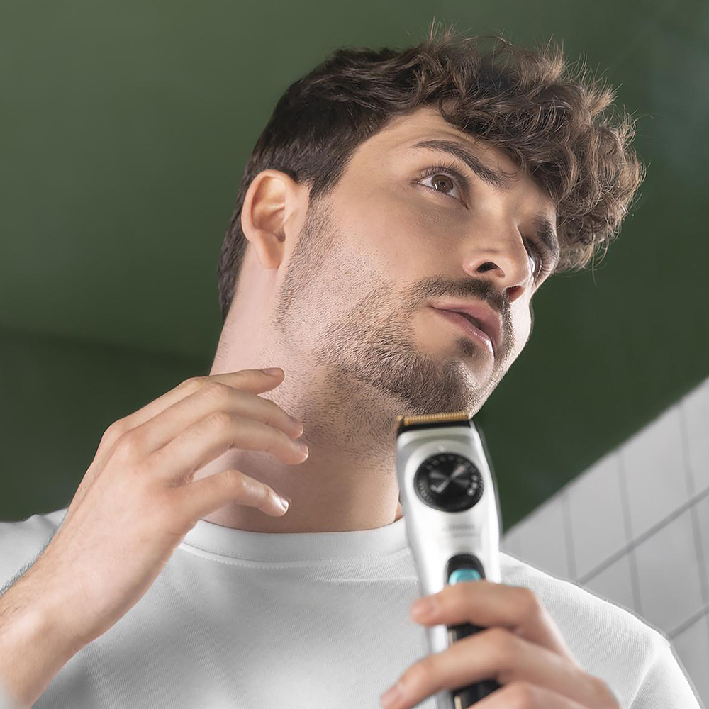 Un joven con cabello castaño se afeita la barba con una recortadora eléctrica gris.