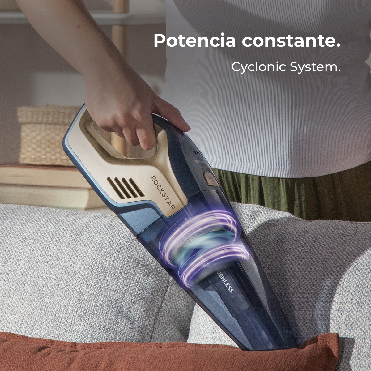 Una persona sostiene una aspiradora de mano portátil sobre un sofá gris.