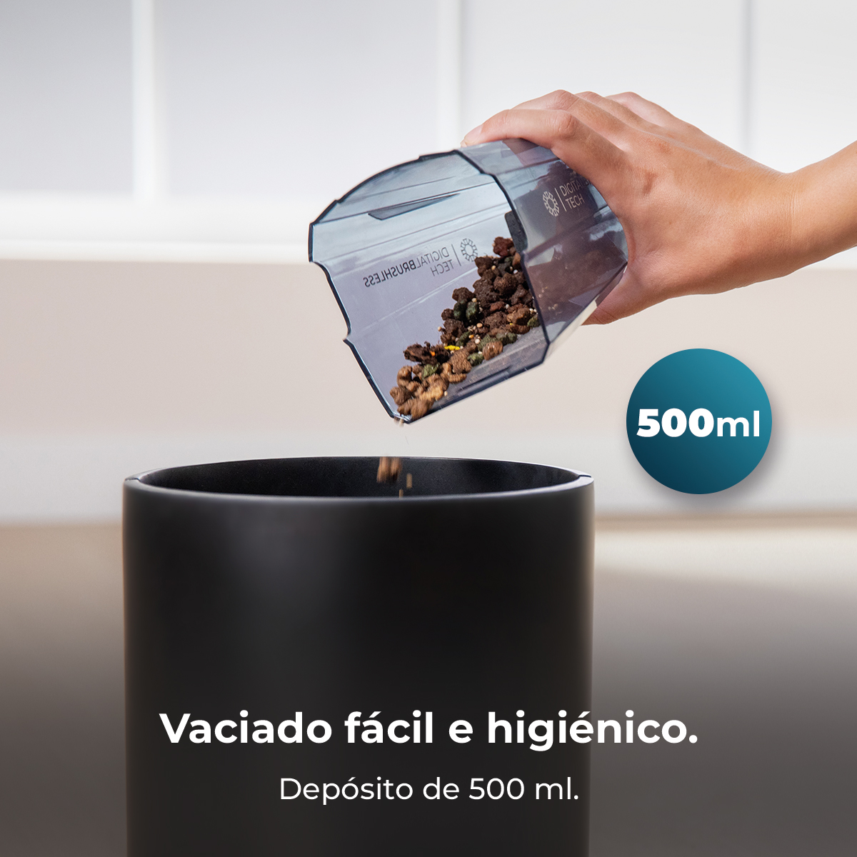 Una mano vacía un depósito transparente de 500 ml lleno de residuos en una papelera negra.