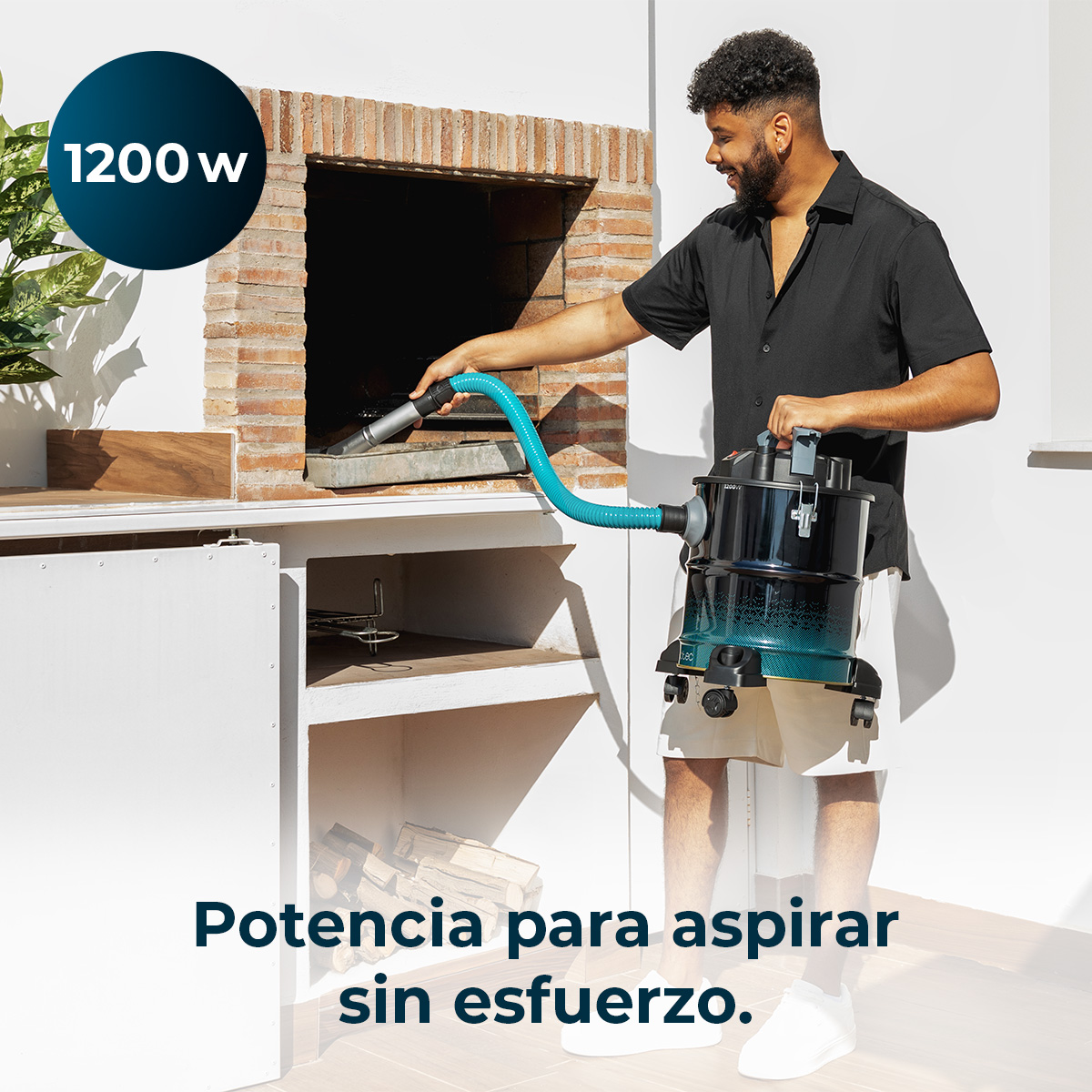 Un hombre usa una aspiradora de cenizas azul para limpiar una chimenea de ladrillo en una terraza soleada.