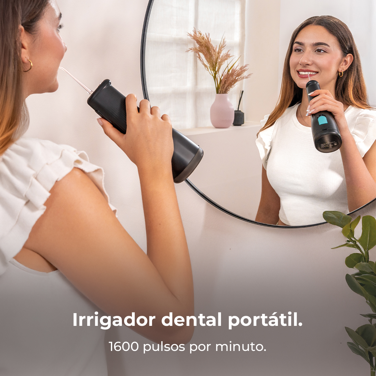 Una mujer usa un irrigador dental portátil frente a un espejo en un baño luminoso.