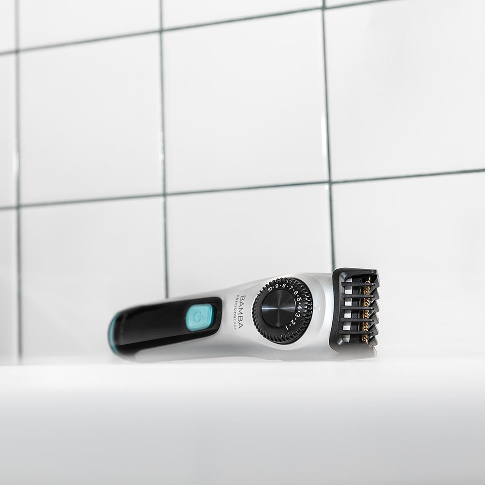 Una recortadora de barba plateada con rueda de ajuste negra ante azulejos blancos.
