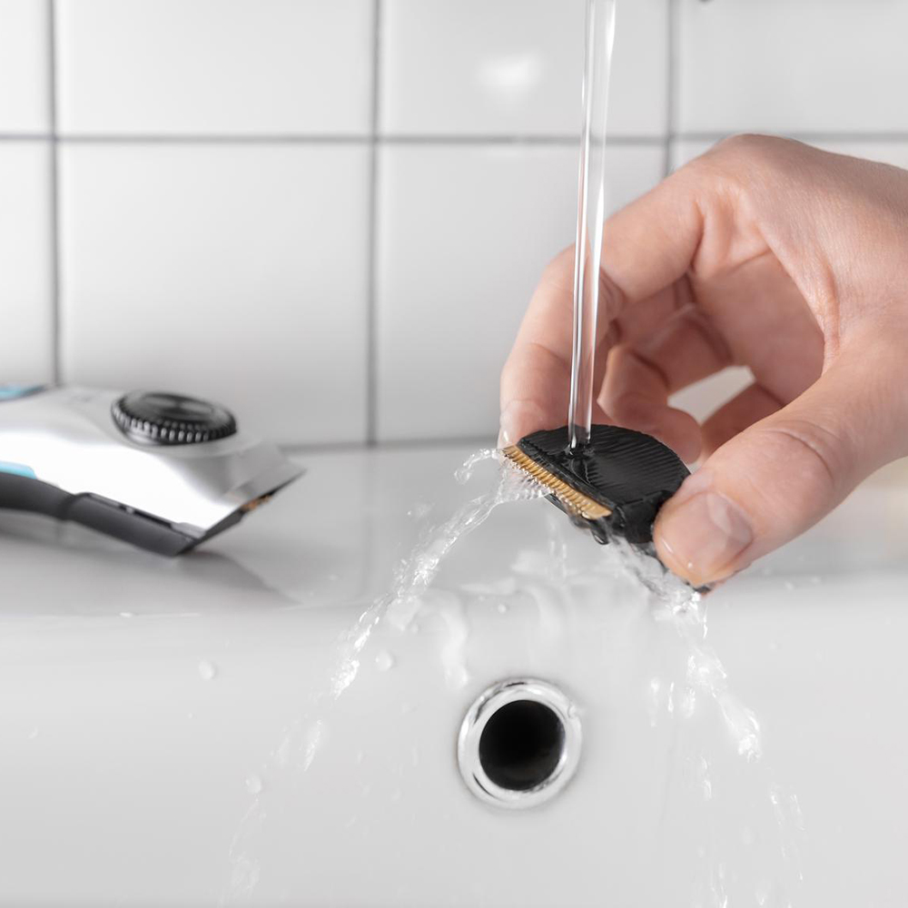 Una mano lava el cabezal de una afeitadora bajo el grifo en un lavabo blanco.