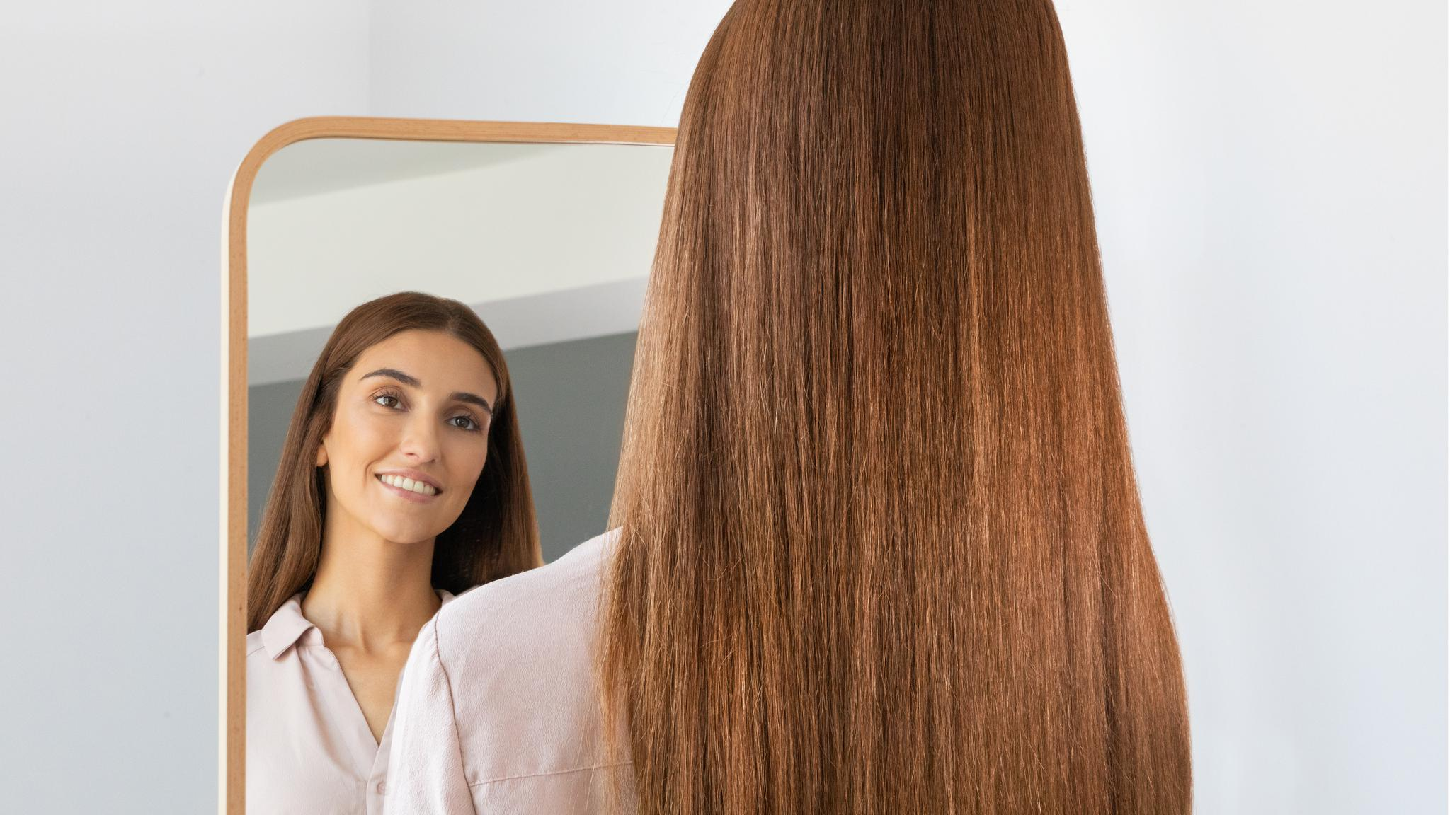 Una mujer con cabello castaño largo se mira en un espejo.