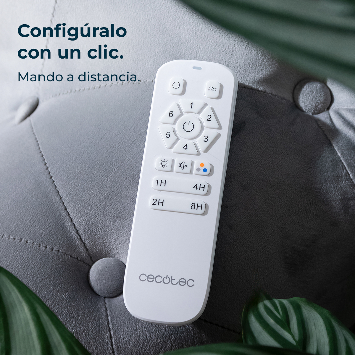 Un control remoto blanco de Cecotec descansa sobre una superficie gris texturizada, rodeado de hojas verdes.