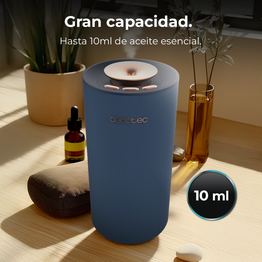 Un difusor de aceite esencial azul en una mesa de madera, con plantas, un cuentagotas y un indicador de 10 ml.