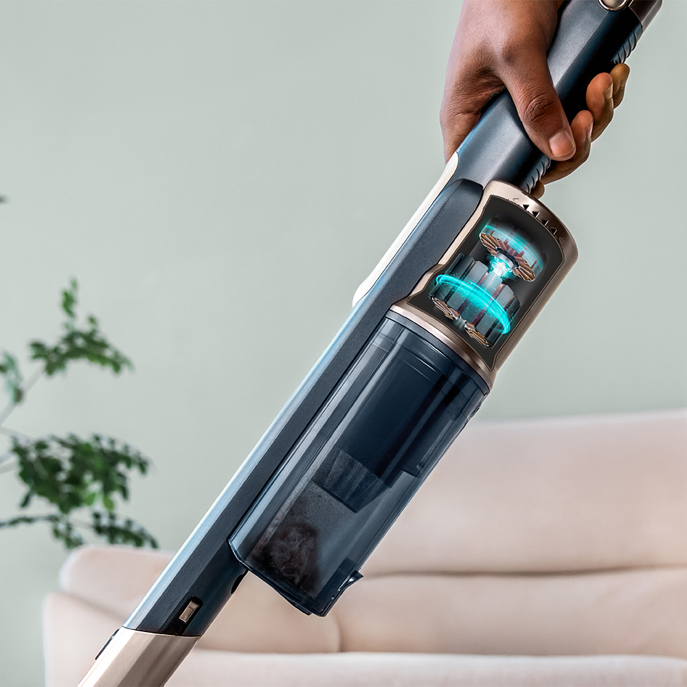 Mano sostiene una aspiradora inalámbrica azul y moderna con motor visible y depósito de polvo en una sala.