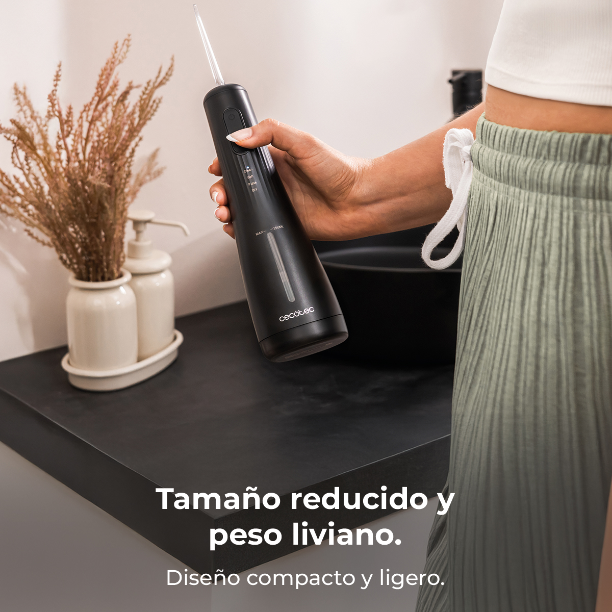 Una mujer sostiene un irrigador bucal negro en un baño luminoso.