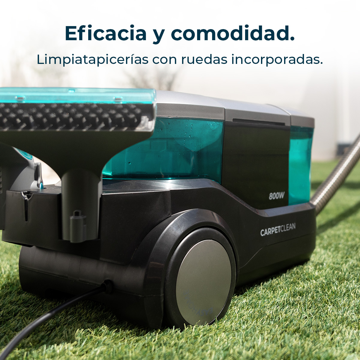 Un limpiador de alfombras negro con un tanque de agua turquesa sobre césped verde.